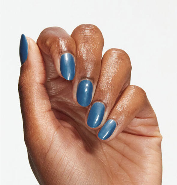 Model's hand wears a medium-dark muted blue shade of nail polish