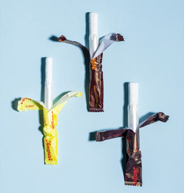 Three august tampons in light, regular, and super absorbencies are unwrapped to show the tampons with applicators inside