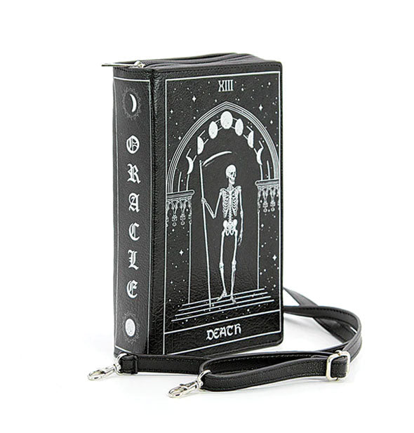 Three-quarter view of a black vinyl "Death" tarot card purse with "Oracle" printed down the spine and featuring a skeleton with celestial design themes; its adjustable strap lays in front