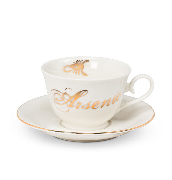 White teacup with "Arsenic" in metallic gold cursive writing and a scorpion graphic on its inner rim sits on a gold-rimmed saucer