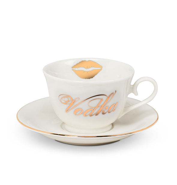 White teacup with "Vodka" in metallic gold cursive and a lips graphic on its inner rim sits on a gold-rimmed saucer