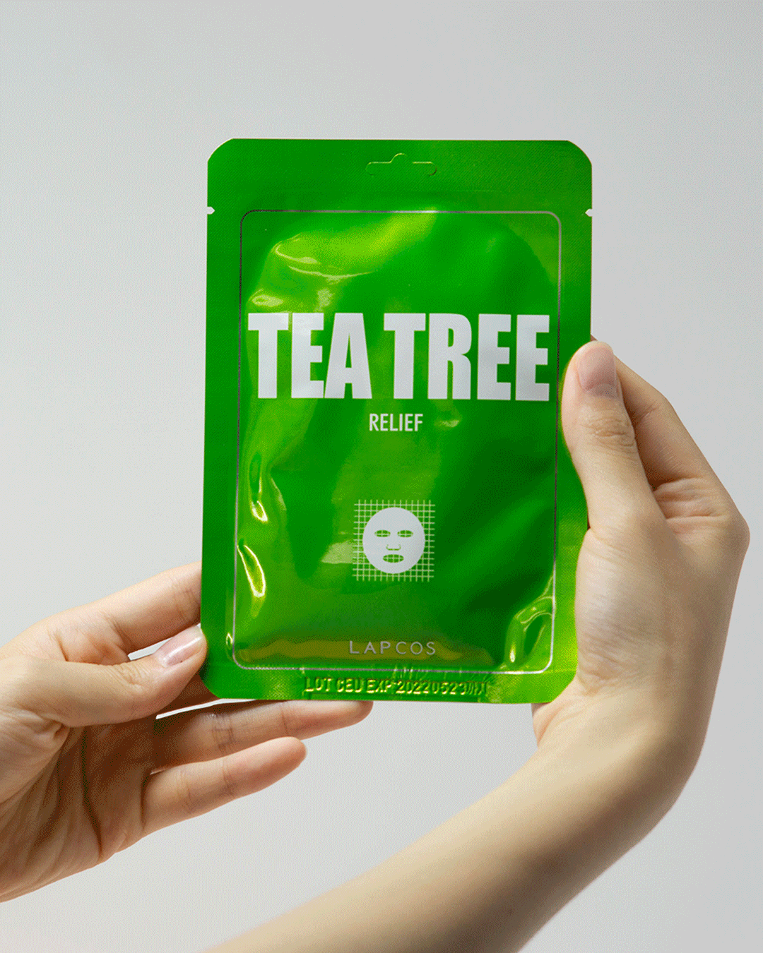 Model opens a Tea Tree Relief mask packet and unfolds the mask inside