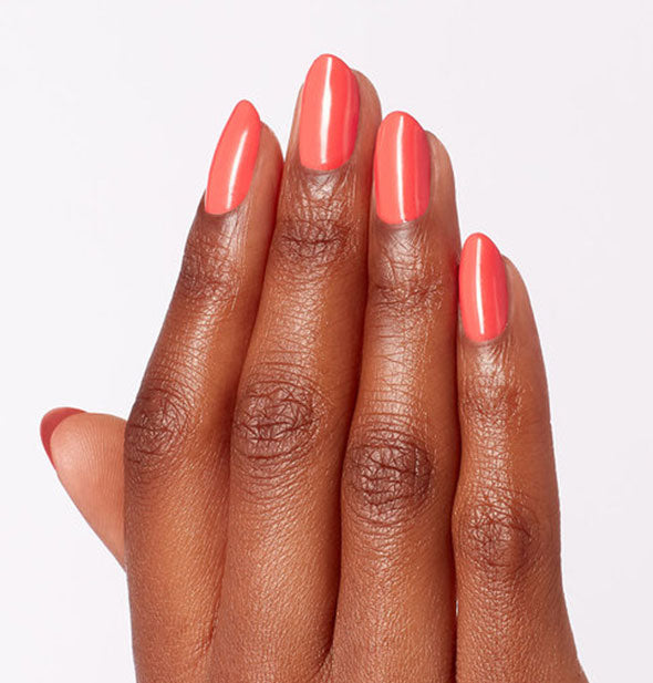 Model's hand wears a soft orange shade of nail polish