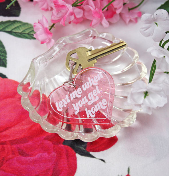 Clear pink glitter keychain laying in crystal seashell dish says, "Text me when you get home" in white lettering