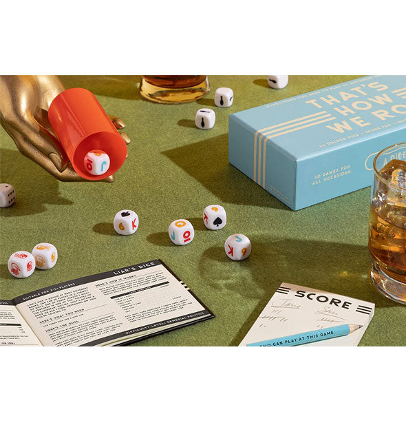 Contents of the That's How We Roll dice game set spread on on a green felt surface staged with whiskey glasses