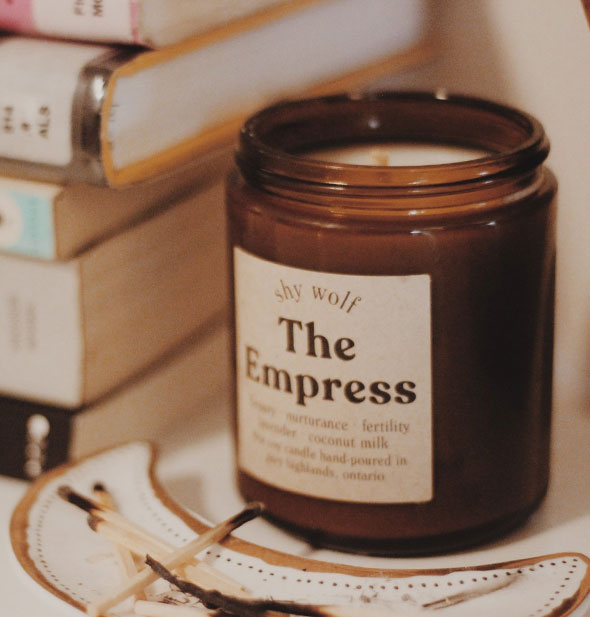 The Empress amber glass jar candle shown with burned matches and a stack of books