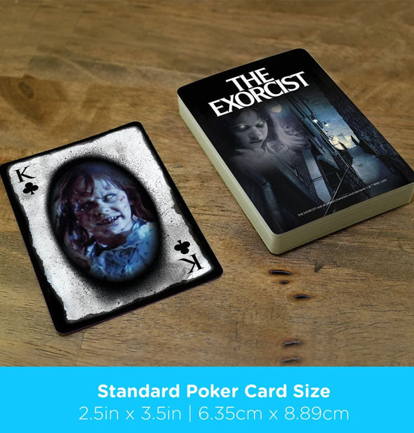 The Exorcist playing card deck with king of clubs on a wooden surface are labeled, "Standard Poker Card Size" with dimensions in inches and centimeters