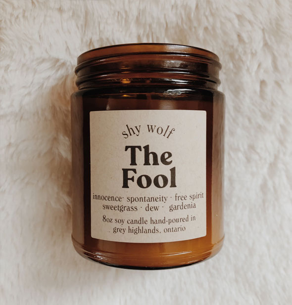 The Fool amber glass jar candle by Shy Wolf rests on a plush white fur background