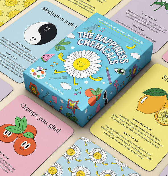 Sample cards from The Happiness Chemicals deck spread out on a tabletop with box in the center