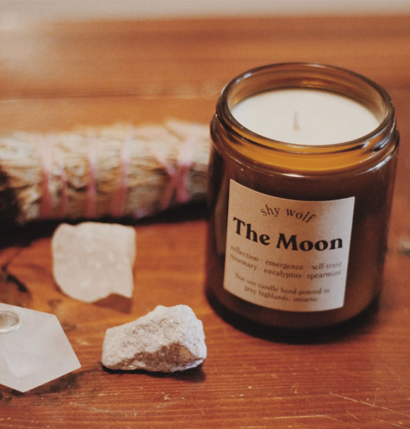 The Moon candle on wooden surface with crystals and a sage bundle