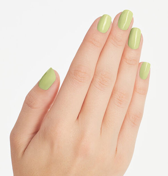 Model's hand wears pastel pea green nail polish