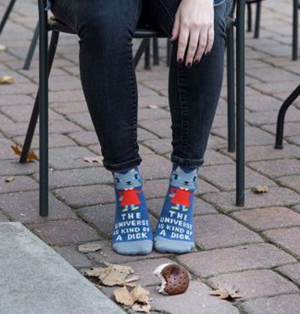 Model wearing The Universe Is Kind of a Dick socks sits on a patio before a dropped ice cream sandwich
