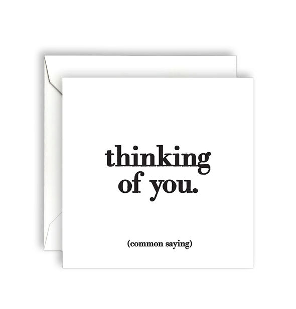 Square white greeting card with envelope is printed in black lettering with the common saying, "Thinking of you."