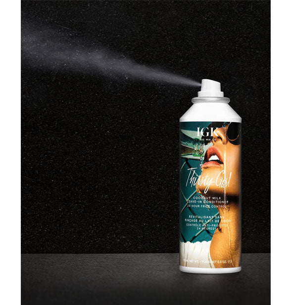 An application of IGK Thirsty Girl Coconut Milk Leave-In Conditioner is dispensed from can in front of a black background to show spray pattern