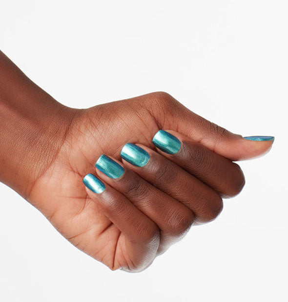 Model's hand wears a reflective, shimmering blue-green nail polish color