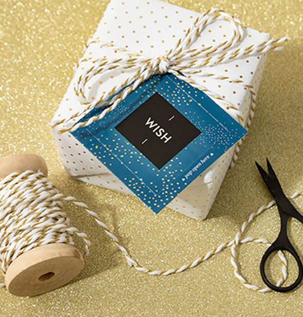 Blue Wish card with gold speckles is attached to a wrapped gift staged with spool of twine and mini scissors