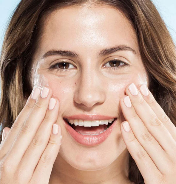 Smiling model applies moisturizer to cheeks