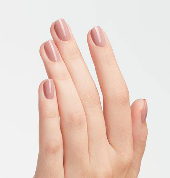 Model's hand wears a rosy nude shade of nail polish