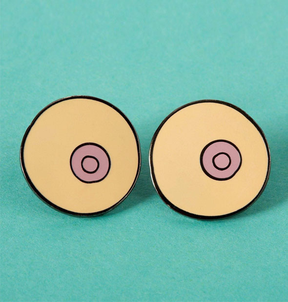 Set of two round boob enamel pins on a teal background