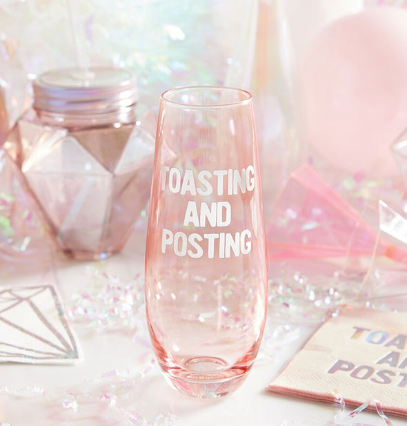 Toasting and Posting pink glass stemless champagne flute sits among pink party accoutrements