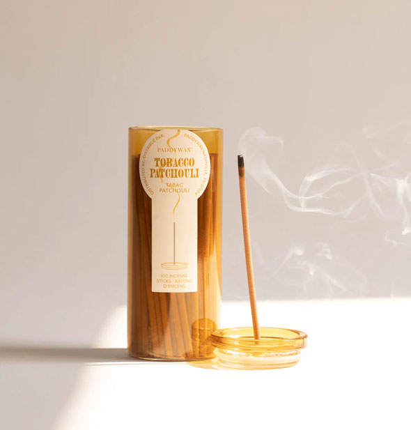Lid removed from a glass tube of Paddywax Tobacco Patchouli incense sticks doubles as a holder for one burning stick