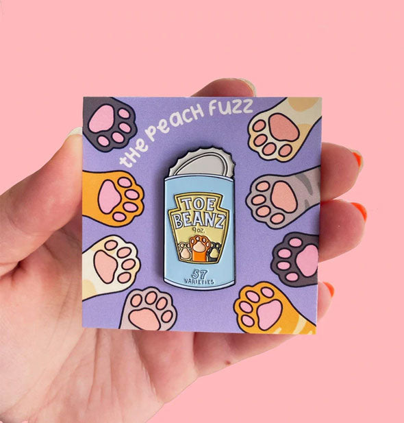 Enamel pin with Heinz imitation "Toe Beanz" label by The Peach Fuzz on card with kitty paw illustrations