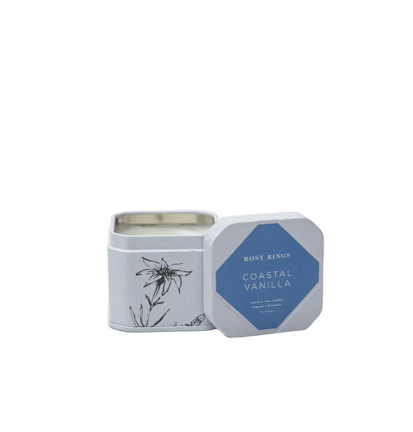 Small white candle tin with beveled corners features a black floral sketch and blue label on the lid that says, "Rosy Rings Coastal Vanilla"
