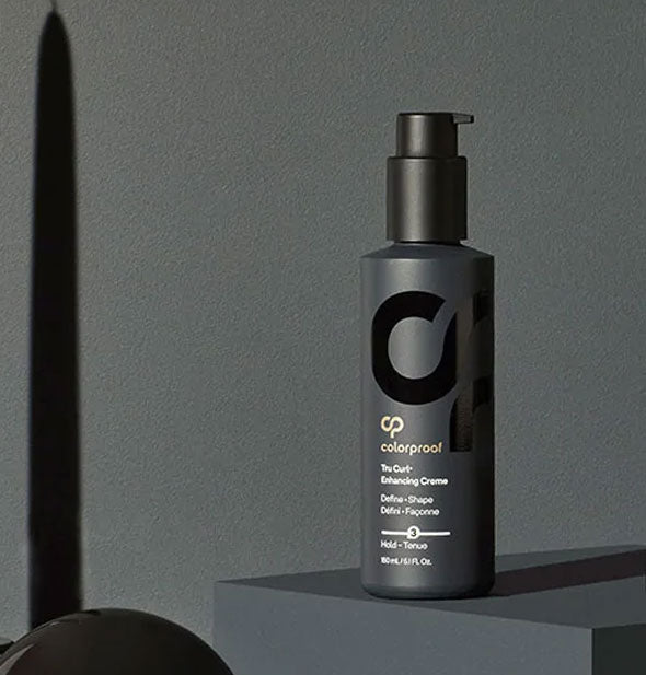 A bottle of ColorProof Tru Curl Enhancing Crème is staged with black shapes and shadows on a black background