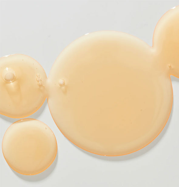 Droplets of peachy-colored Unite U Argan Oil with some bubbles