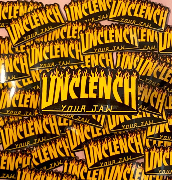 A pile of Unclench Your Jaw stickers with one pulled to the foreground