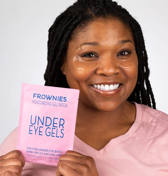 Smiling model wears a pair of Frownies Under Eye Gels and holds packaging forward