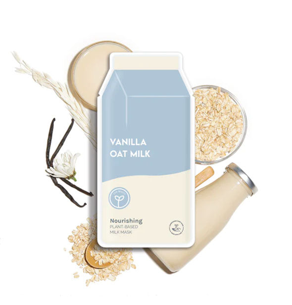 Carton-shaped Vanilla Oat Milk sheet mask packet rests on top of loose oats, vanilla beans, and a glass milk bottle