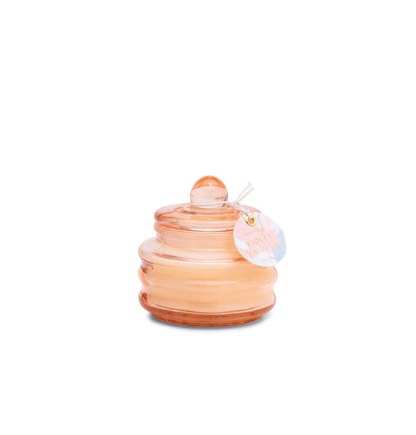 Small peach-colored ribbed glass candle jar with knobbed lid and tag attached