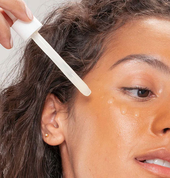 Model applies droplets of facial serum to cheek with a dropper applicator