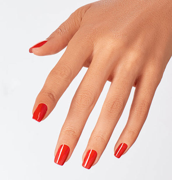 Model's hand wears a red-orange shade of nail polish