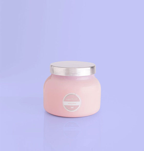 Small pink glass jar candle with silver lid and white label on a purple background