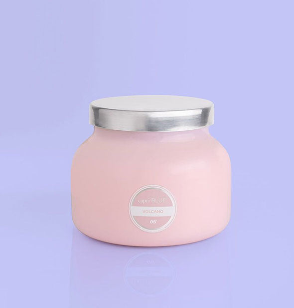 Pink glass jar candle with silver lid and white label on a purple background