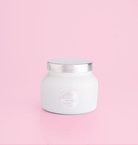 Small white glass jar candle with silver lid and label on a pink background