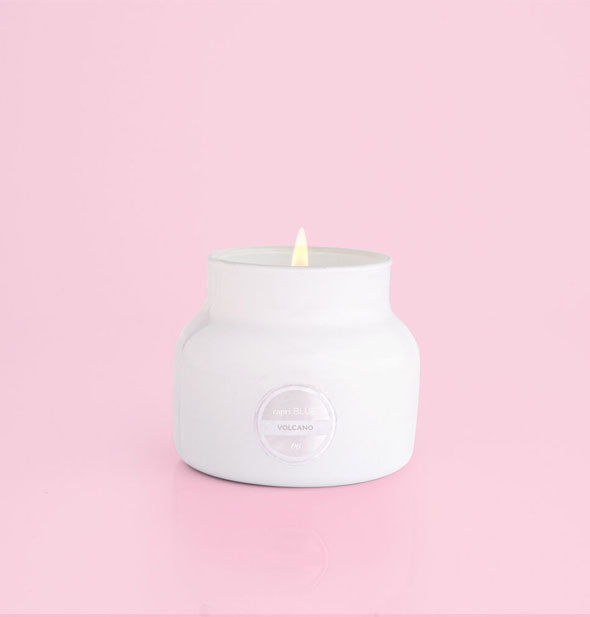 Lit white glass jar candle on a pink background