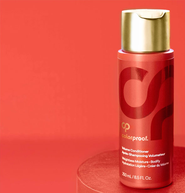 Bottle of ColorProof Volume Conditioner sits on a circular red surface against a red background