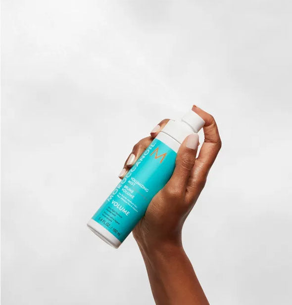 Model's hand dispenses and spritz of Moroccanoil Volumizing Mist into the air