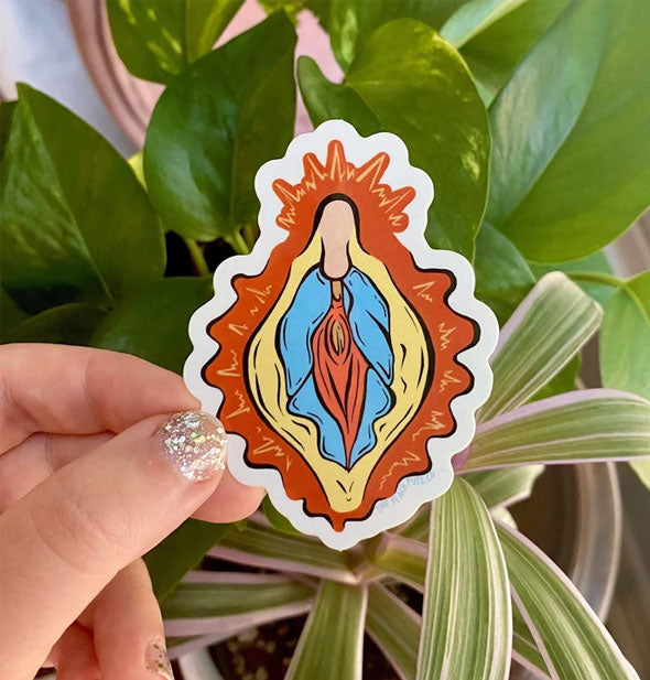 Model's hand holds a sticker with colorful, stylized design of vulvar anatomy on a leafy backdrop