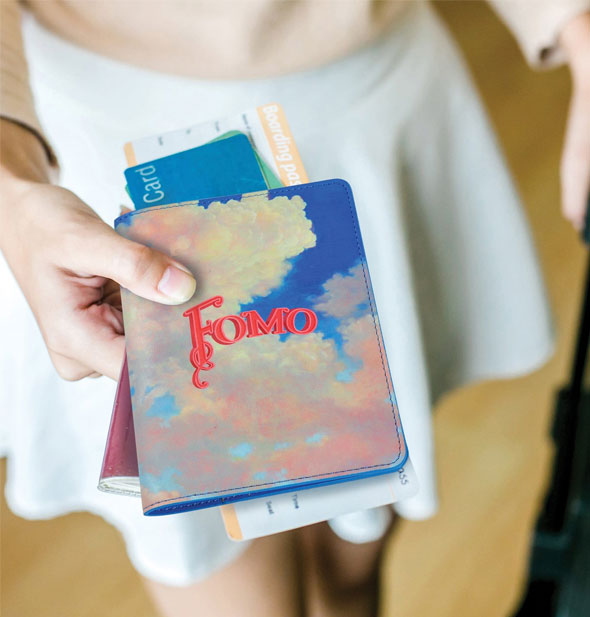 Model holds out the FOMO passport wallet with other documents under and emerging from it