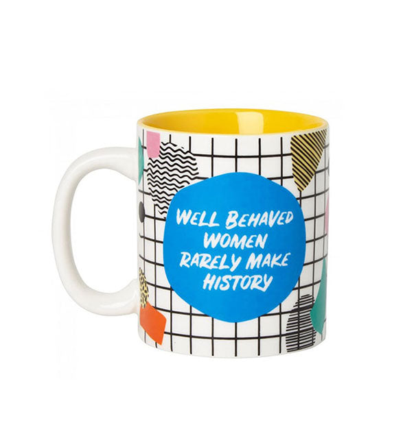 White coffee mug with yellow interior and all-over colorful geometric shapes and checker pattern says, "Well behaved women rarely make history" in the center of a blue circle
