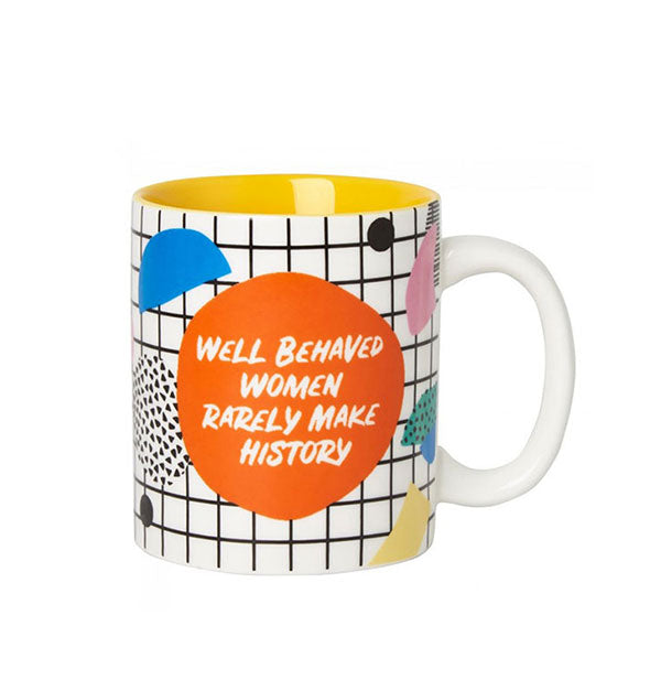 White coffee mug with yellow interior and all-over colorful geometric shapes and checker pattern says, "Well behaved women rarely make history" in the center of an orange circle