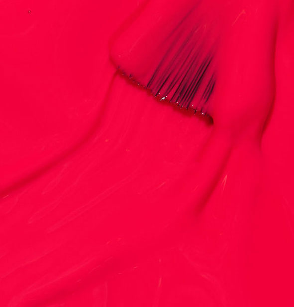 Vibrant reddish, pinkish orange nail polish with brush tip dipped in