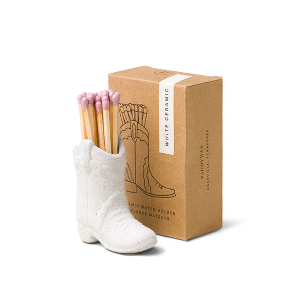 White ceramic cowboy boot match holder with pink-tipped wooden matches inside next to brown box packaging