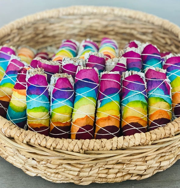 A basket is filled with neat rows of colorful rose petal-wrapped sage smudge sticks