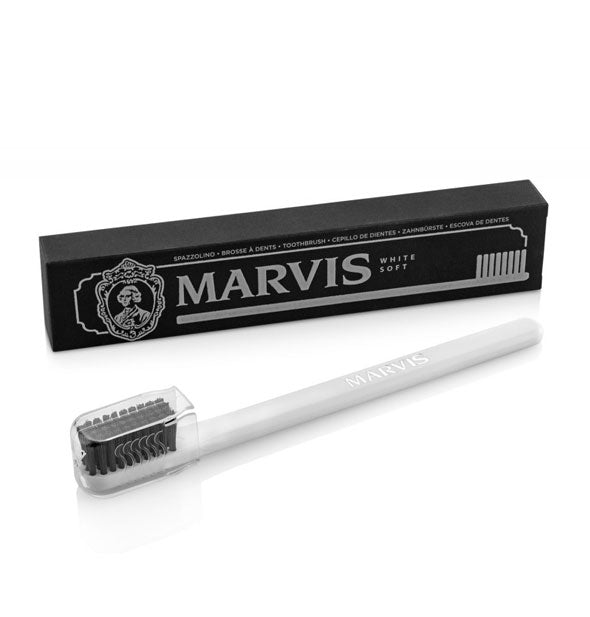 White Marvis toothbrush with black bristles covered with clear plastic protector sits alongside black box packaging