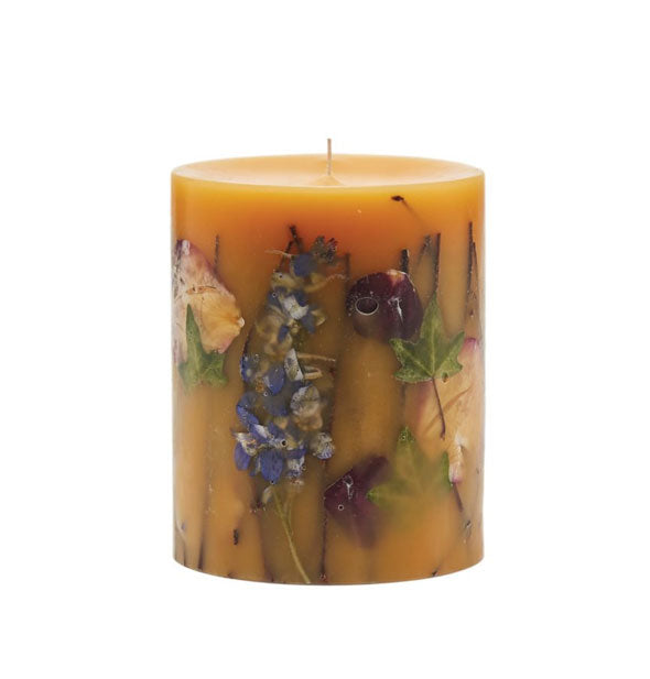 Amber pillar candle with various flowers, leaves, and twigs embedded in the wax